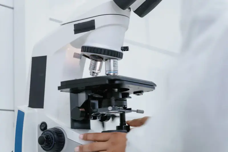 White research microscope with a hand adjusting the focus knob