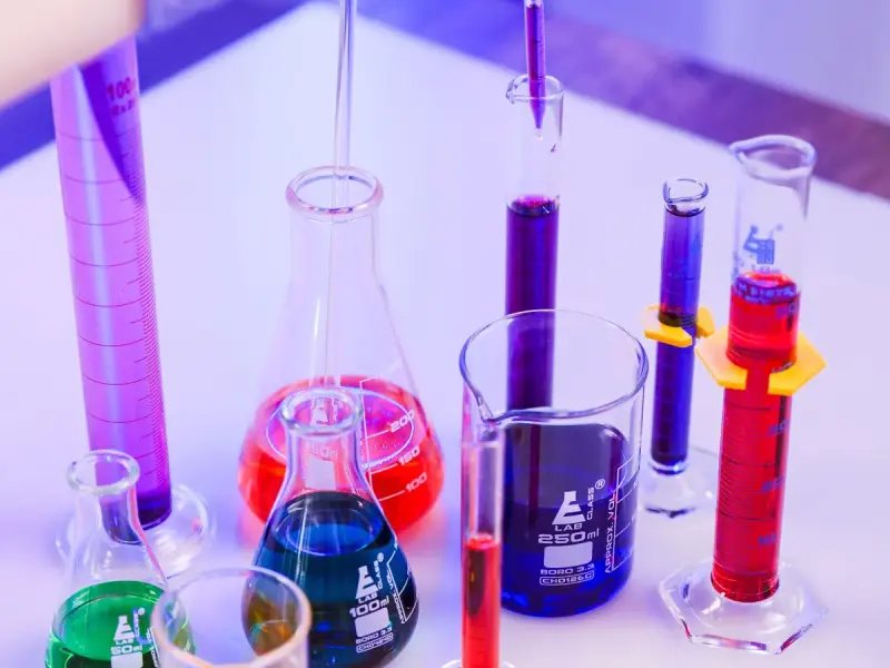 Erlenmeyer flask, beakers and cylinders filled with blue, red and purple liquids under violet light