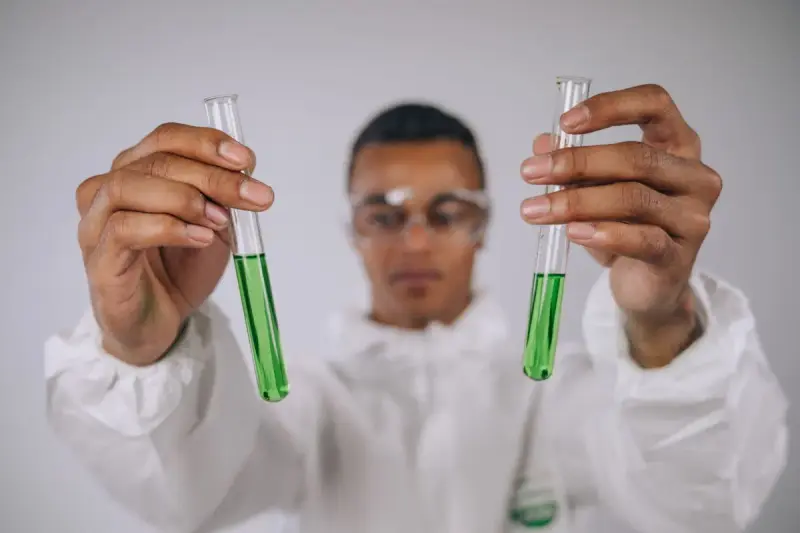 Scientist in safety glasses holding up two test tubes of green liquid