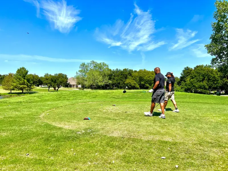Two golfers walking down a sunny fairway in North Texas with trees behind