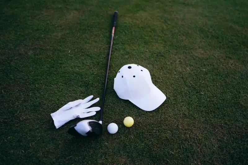 Golf club, white glove, cap and balls laid out on green grass