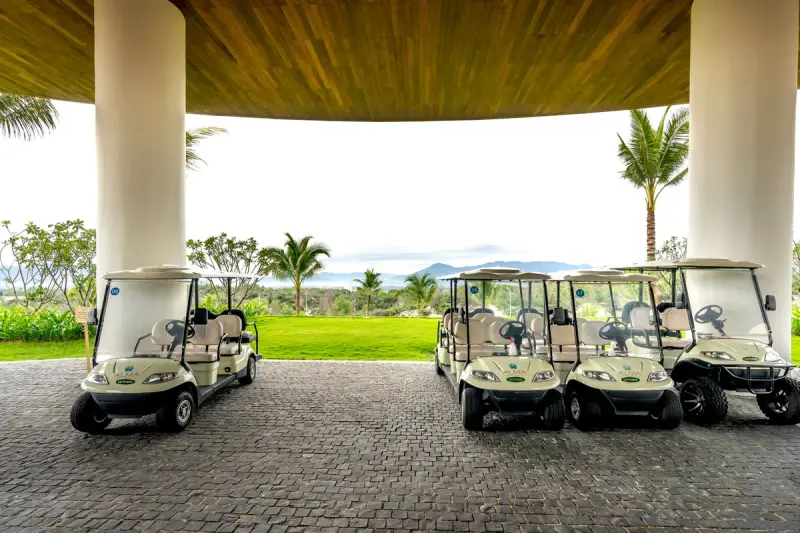 Row of white golf carts parked under a resort portico facing the course