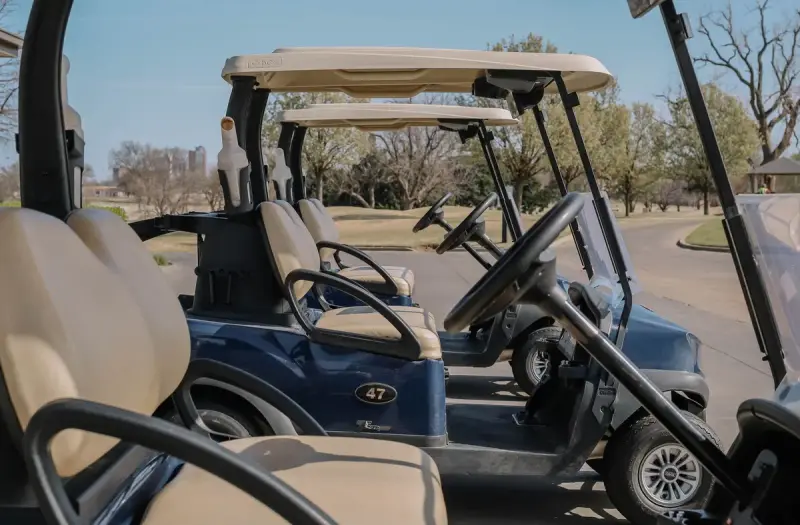 Row of golf carts parked in the sun on a cart path