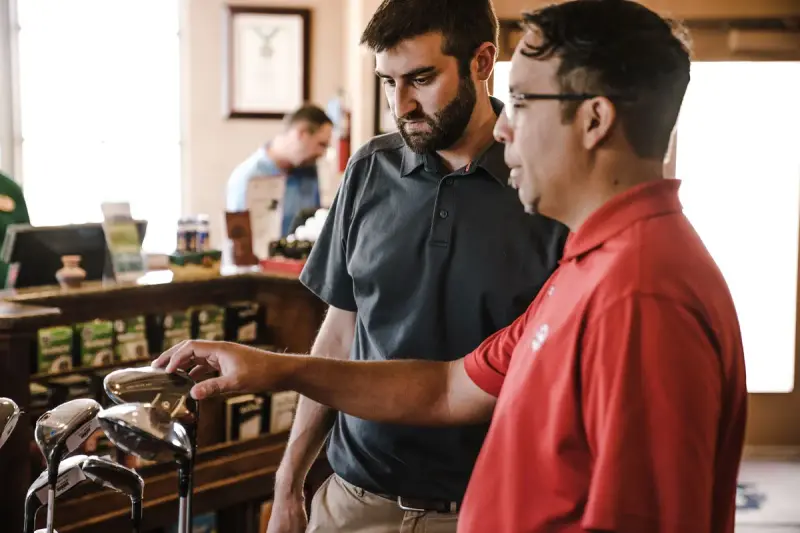 Pro-shop staff member showing a customer a set of irons on a display rack