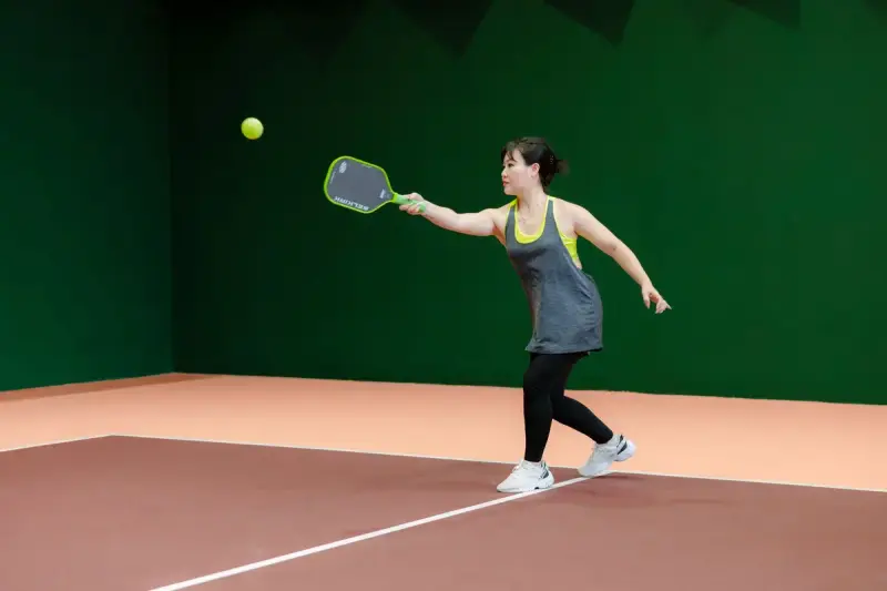 Woman hitting a pickleball forehand on an indoor court
