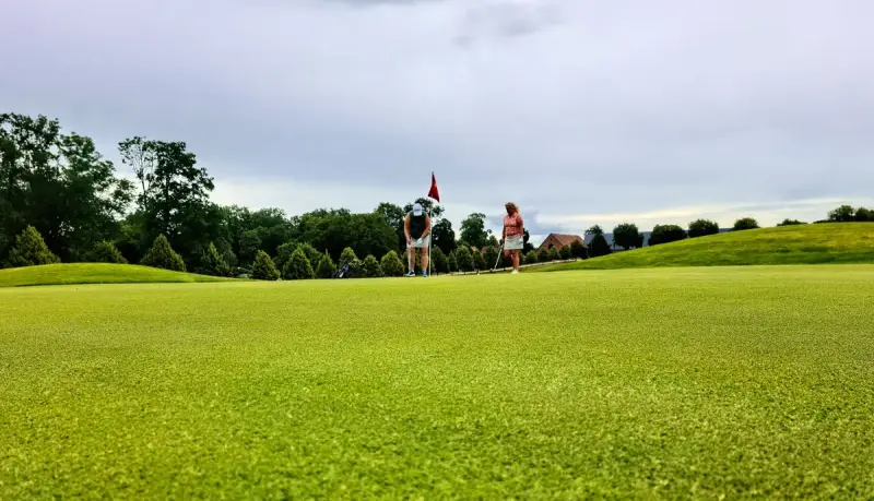 Two women playing golf on a green with a flag and rolling fairways behind them