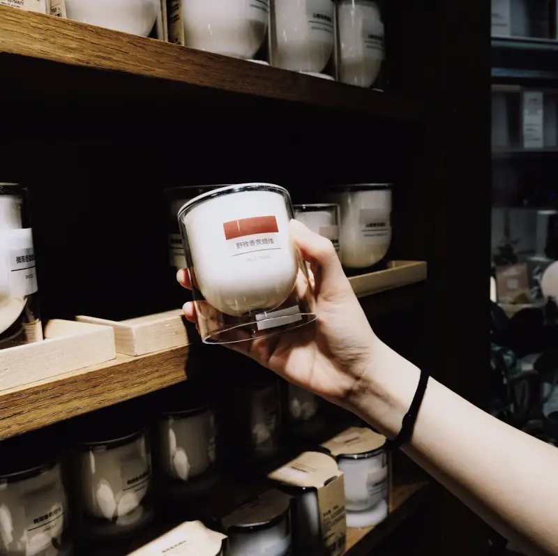 Hand picking a scented candle in a glass tumbler from a shop shelf