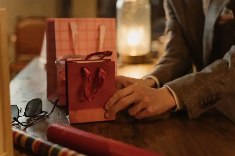 Hands arranging small paper gift bags on a wooden table