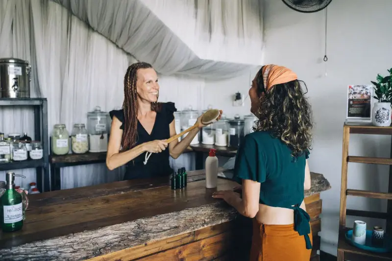 Smiling shop owner showing a bath brush to a customer across the counter
