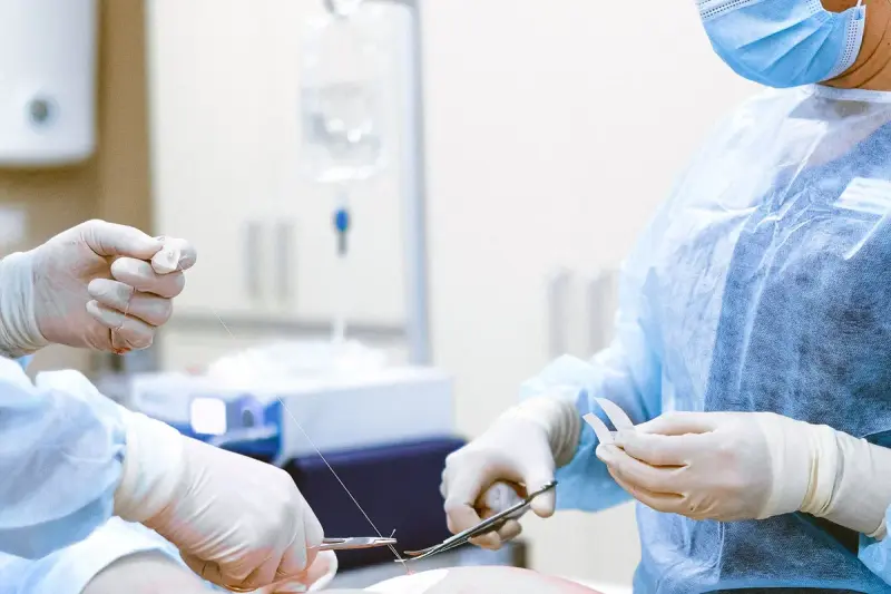 Gloved hands of two surgeons holding a needle holder and suture during a procedure