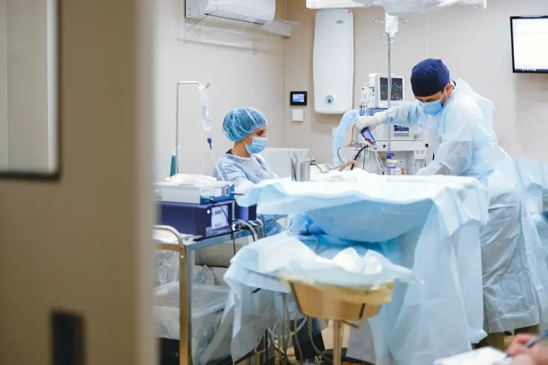 A woman nurse and a male surgeon in scrubs and masks preparing an operating room