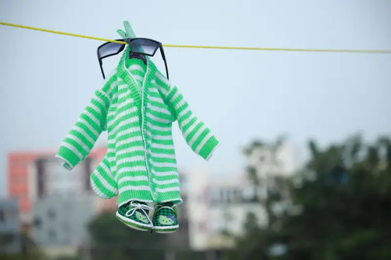Green striped baby outfit with tiny sunglasses and shoes on a clothesline