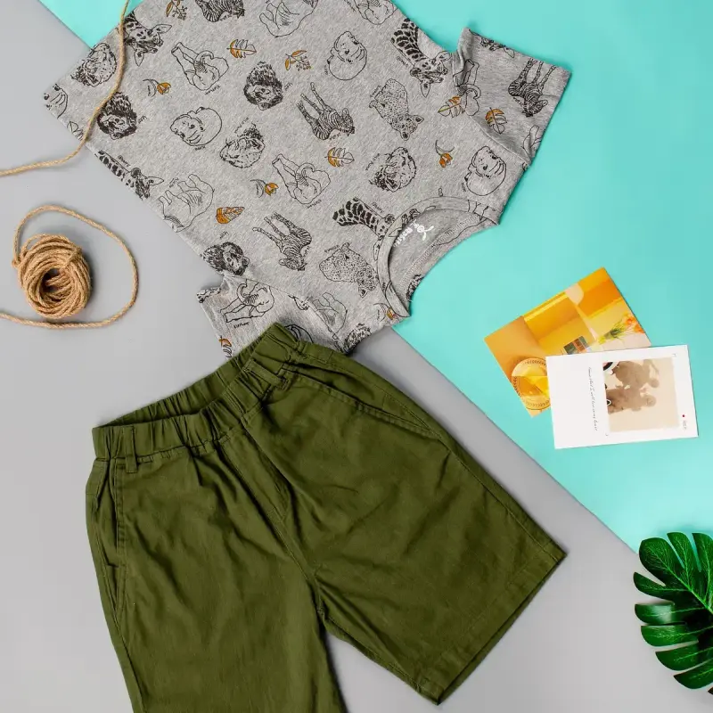 Flat lay of a boy's printed gray tee and olive shorts with twine and cards on mint and gray