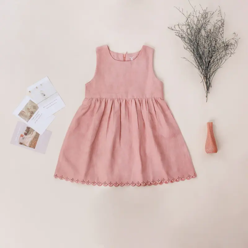 Flat lay of a girl's pink linen sundress with postcards and dried flowers on beige