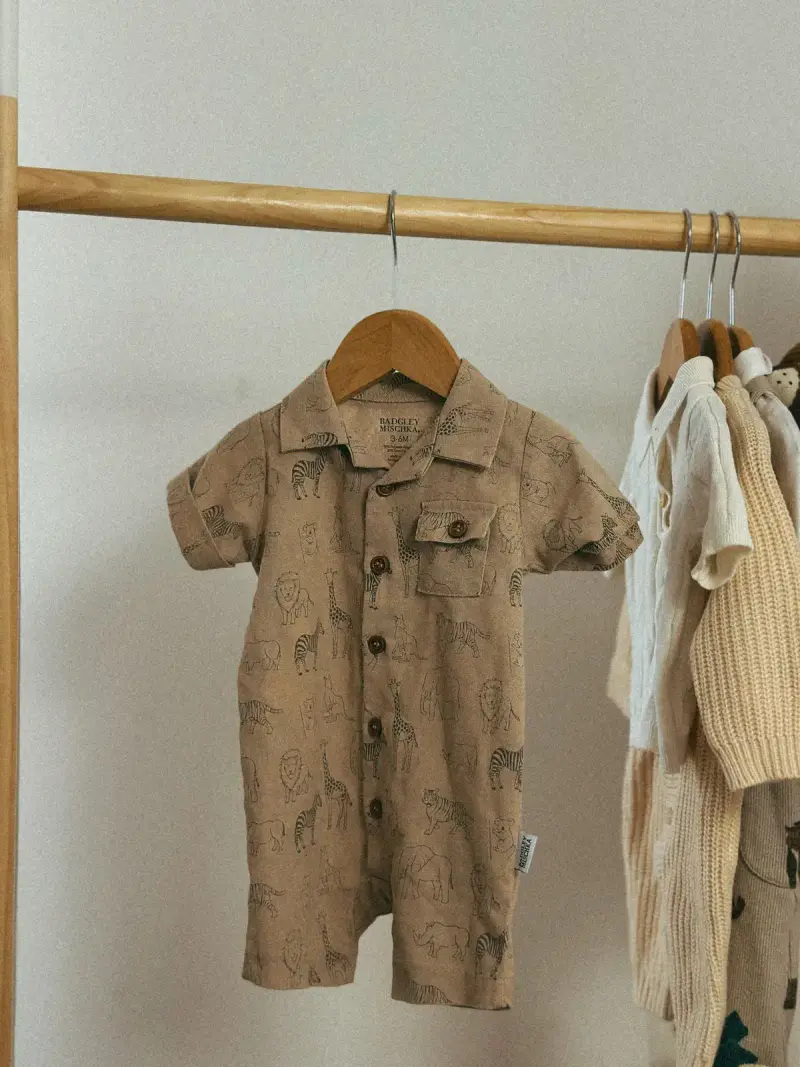 Neutral printed baby romper on a wooden hanger beside cream knits on a rail