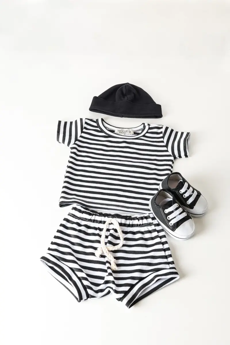 Black and white striped baby outfit with tiny sneakers and a hat on white