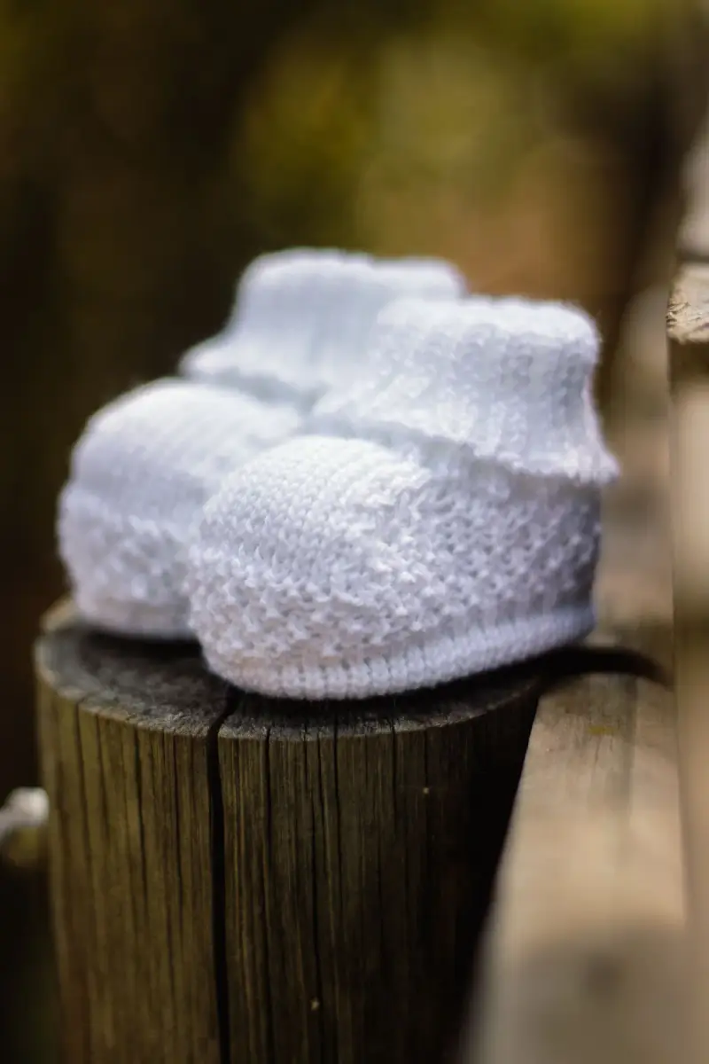 White knitted baby booties on a wooden stump
