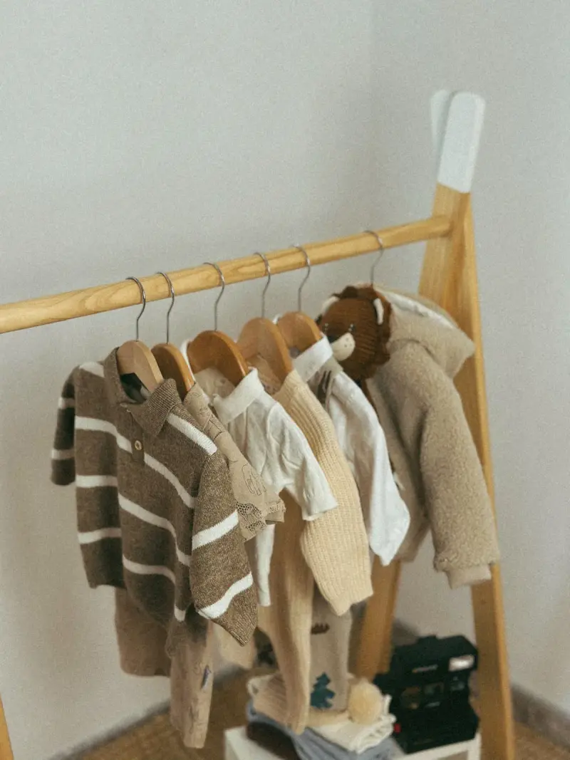 Knitted baby sweaters in brown and cream on a small wooden rack