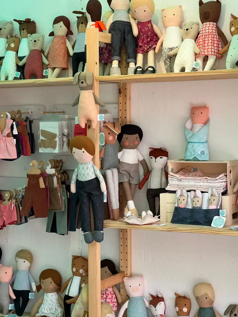 Handmade cloth dolls and small clothes on wooden shelves in a shop