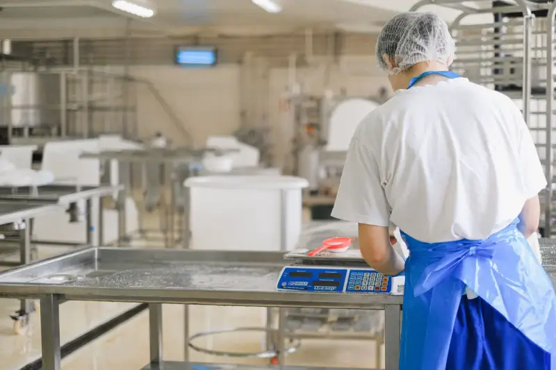 Factory worker in uniform weighing ingredients on a digital scale