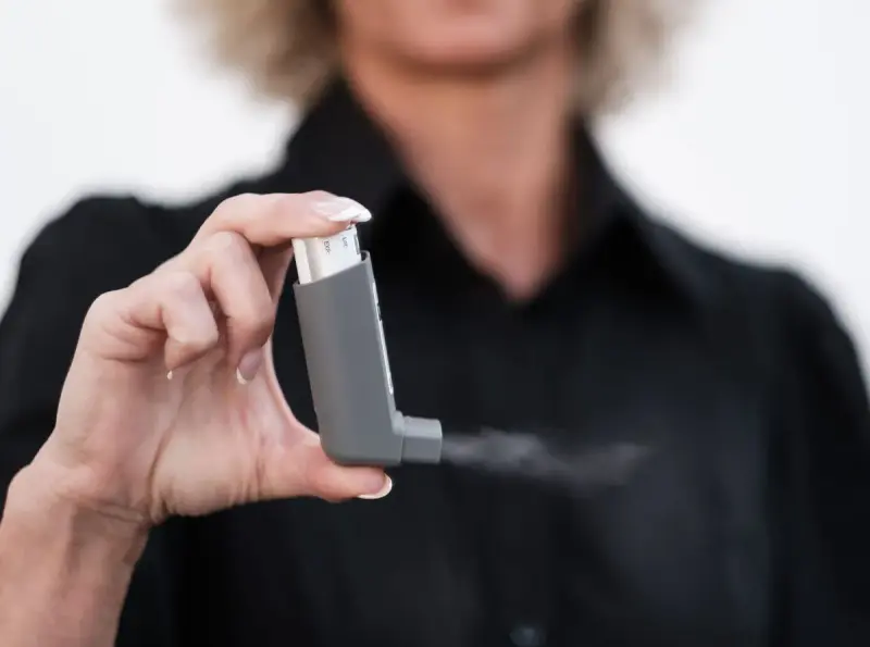 Hand holding a grey metered-dose inhaler releasing a fine mist