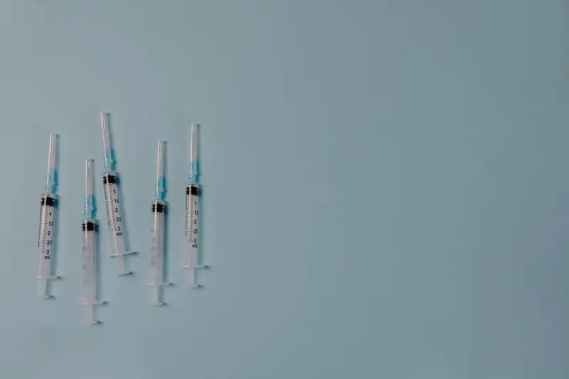 Six disposable syringes laid out on a light blue-grey surface