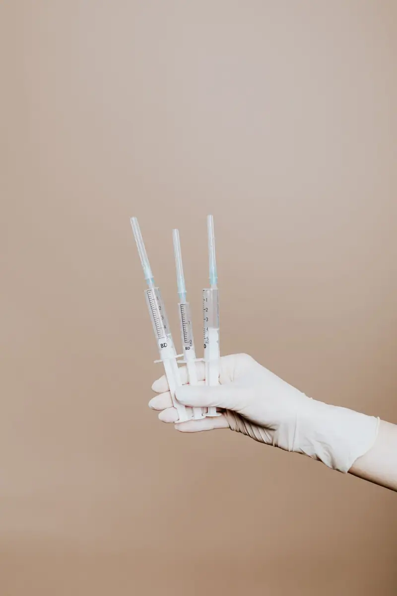 Gloved hand holding three filled syringes against a beige background