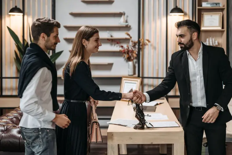 Man in a suit shaking hands with a woman beside her colleague in a modern office