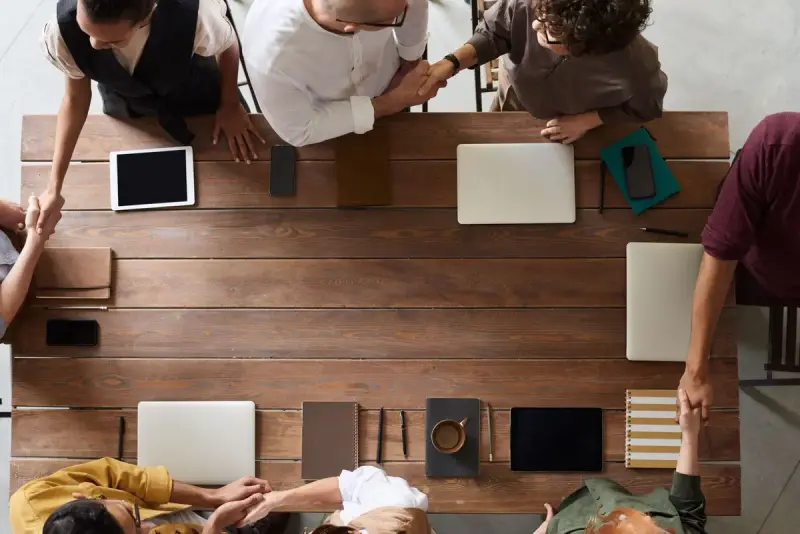 Overhead view of a team meeting around a wooden table with laptops and tablets