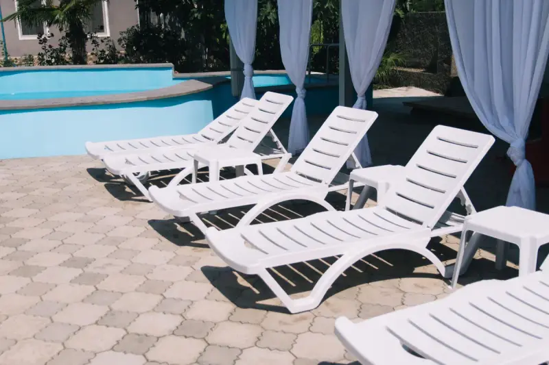 White lounge chairs and cabana curtains beside a resort pool on paver tiles