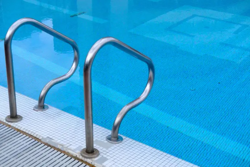 Stainless steel ladder rails entering a blue tiled swimming pool
