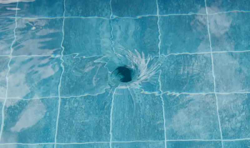 Swirling vortex over a drain in clear water above blue pool tiles