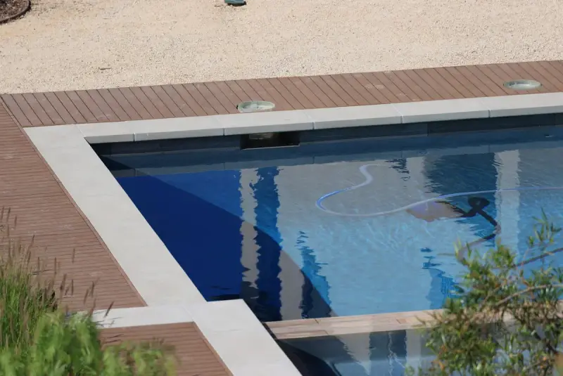 Pool cleaner hose lying in a blue pool edged with wooden decking