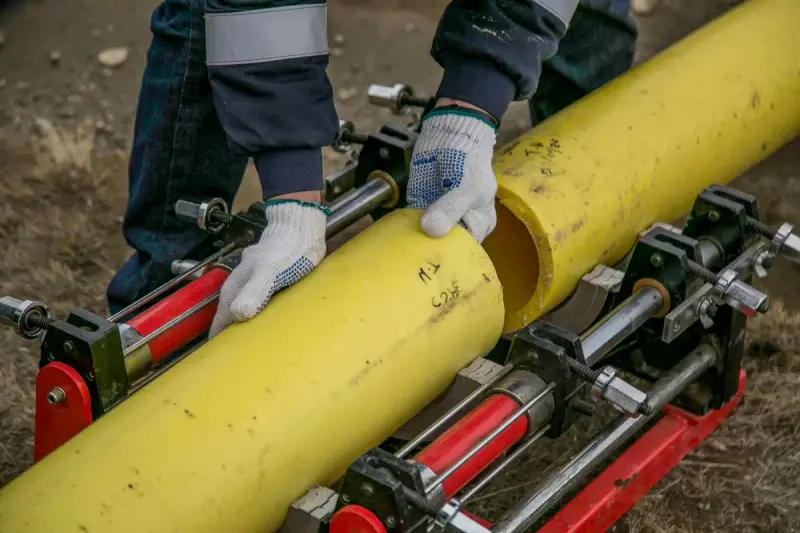 Gloved workers clamping a yellow pipe in a fusion machine outdoors