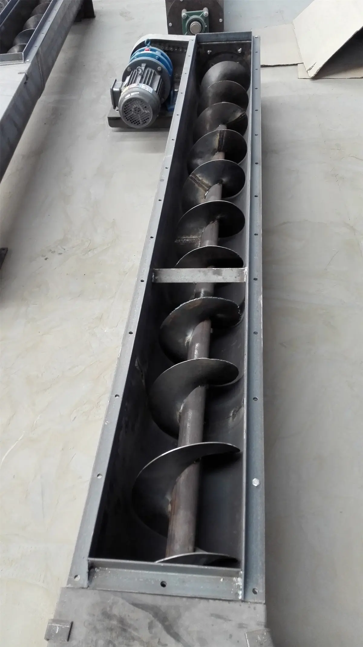 An exposed screw conveyor, shown lengthwise; bulk handling equipment reference.