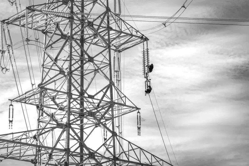 Black and white view of workers on a steel transmission tower against a cloudy sky