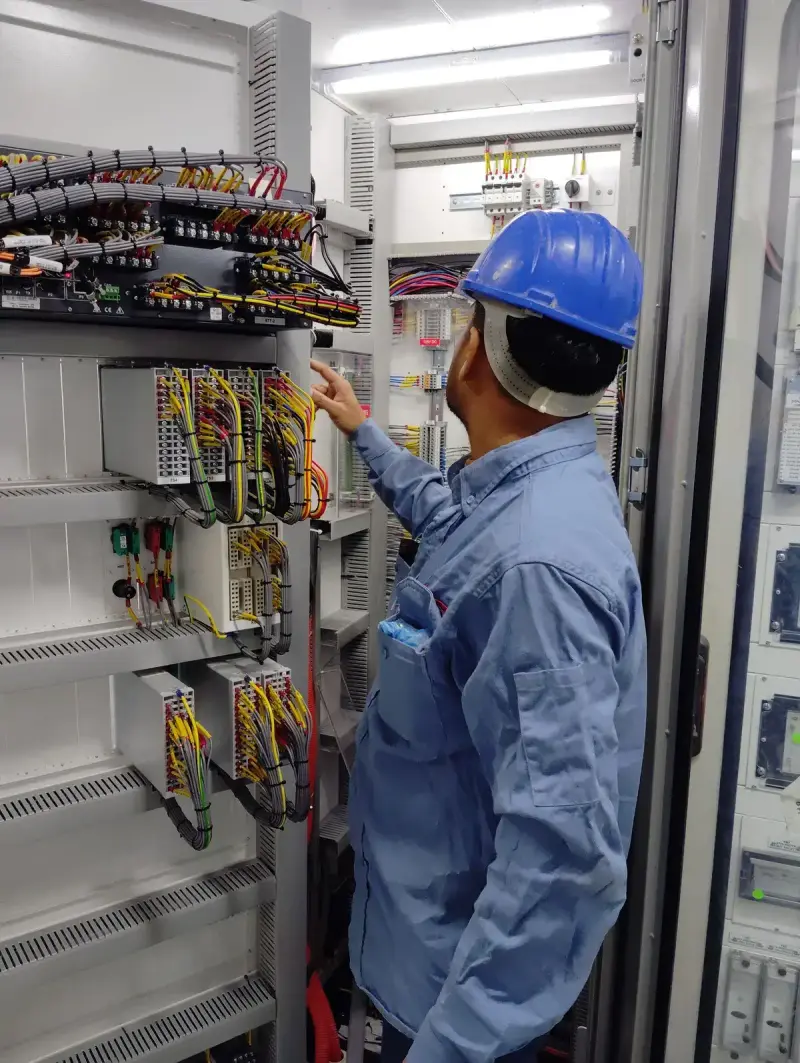 Electrician in a hard hat inspecting wiring inside an industrial control panel