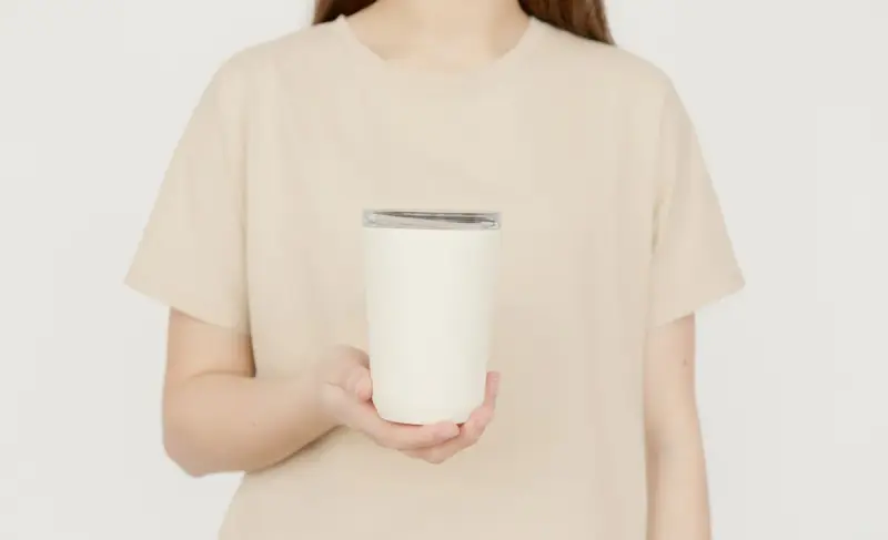 Person in a beige t-shirt holding a blank white insulated tumbler