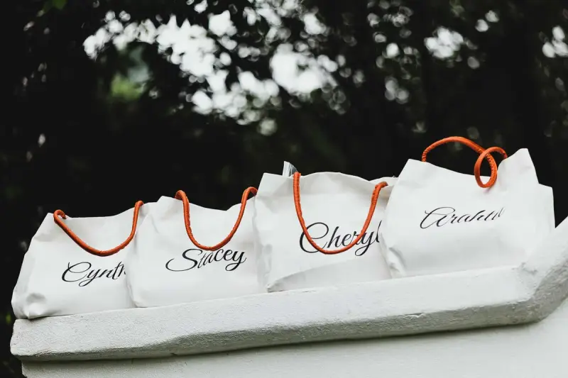 Four white canvas tote bags with orange handles, each personalized with a name