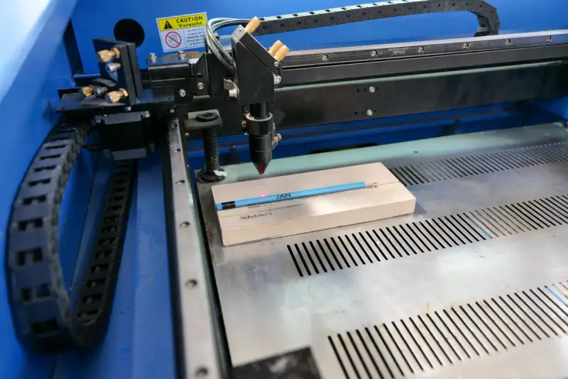 Laser engraving machine head working over a wooden pencil on its cutting bed