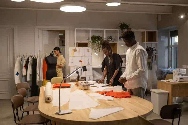 Design team laying out garments and patterns on a large table in a bright studio