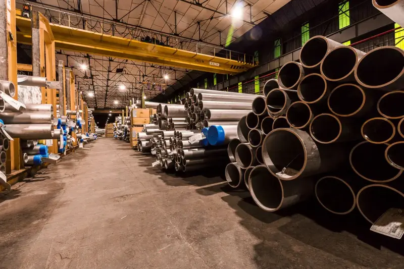 Long warehouse aisle lined with stacks of large steel pipes