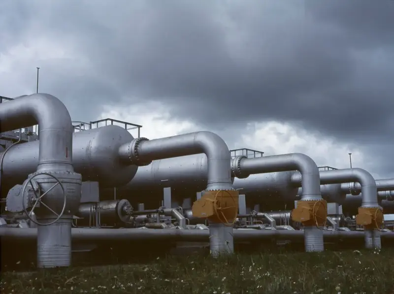 Steel pipes and valves at an above-ground station under dark storm clouds