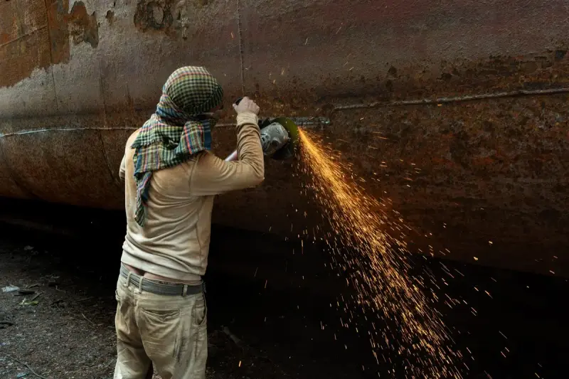 Worker grinding a large rusty pipe with sparks streaming from the disc