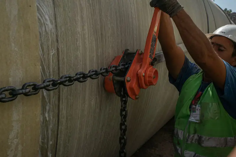Worker using a chain lever hoist on a large pipe section