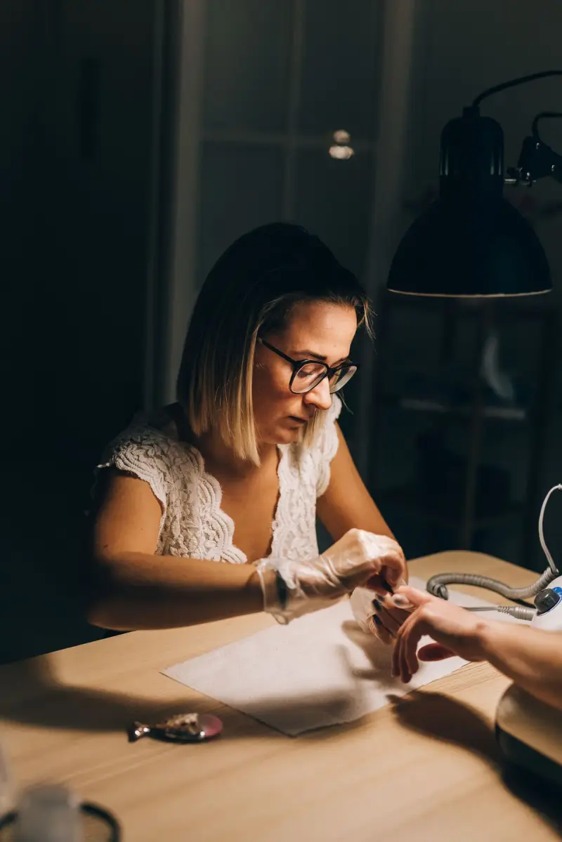 Nail technician giving a manicure under a warm desk lamp