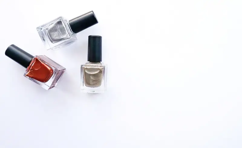 Three nail polish bottles in metallic and red shades on a white background