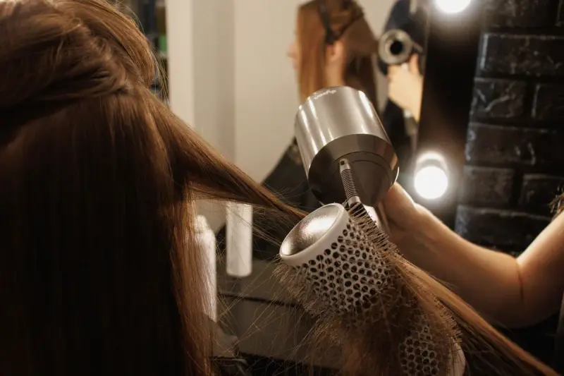 Stylist blow-drying a client's long hair with a round brush in a salon