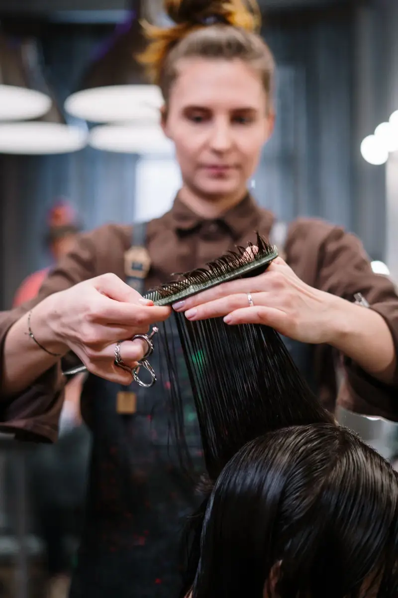 Stylist in a brown apron cutting a client's wet hair with comb and shears