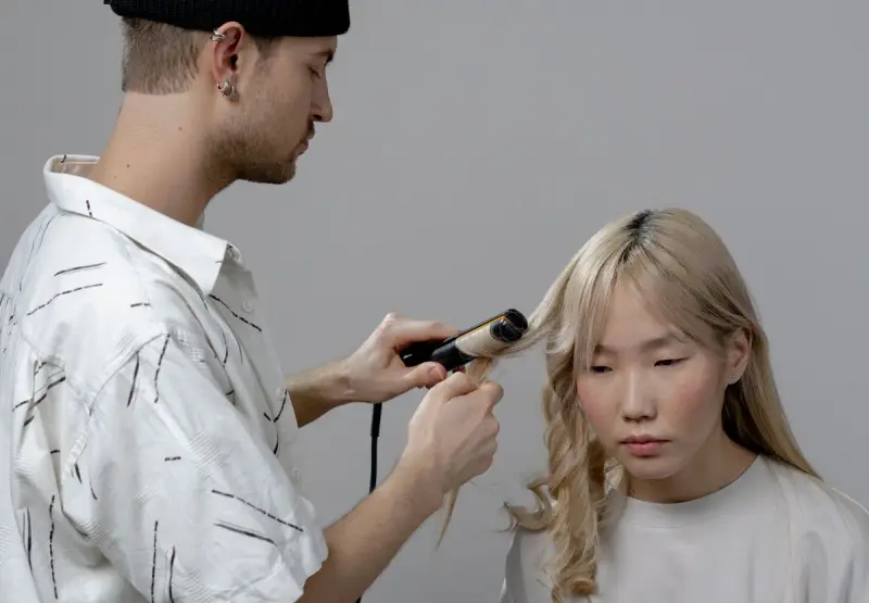 Stylist using a curling iron on a client's long blonde hair